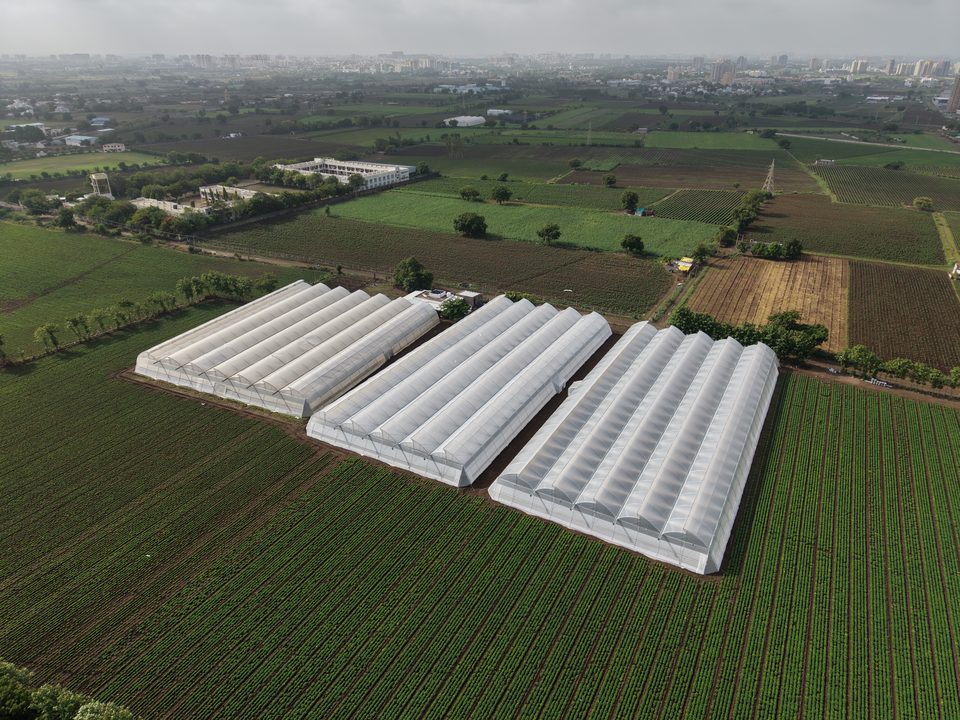 Three Avishkar Agribiz polyhouses seen from the air across open farmland